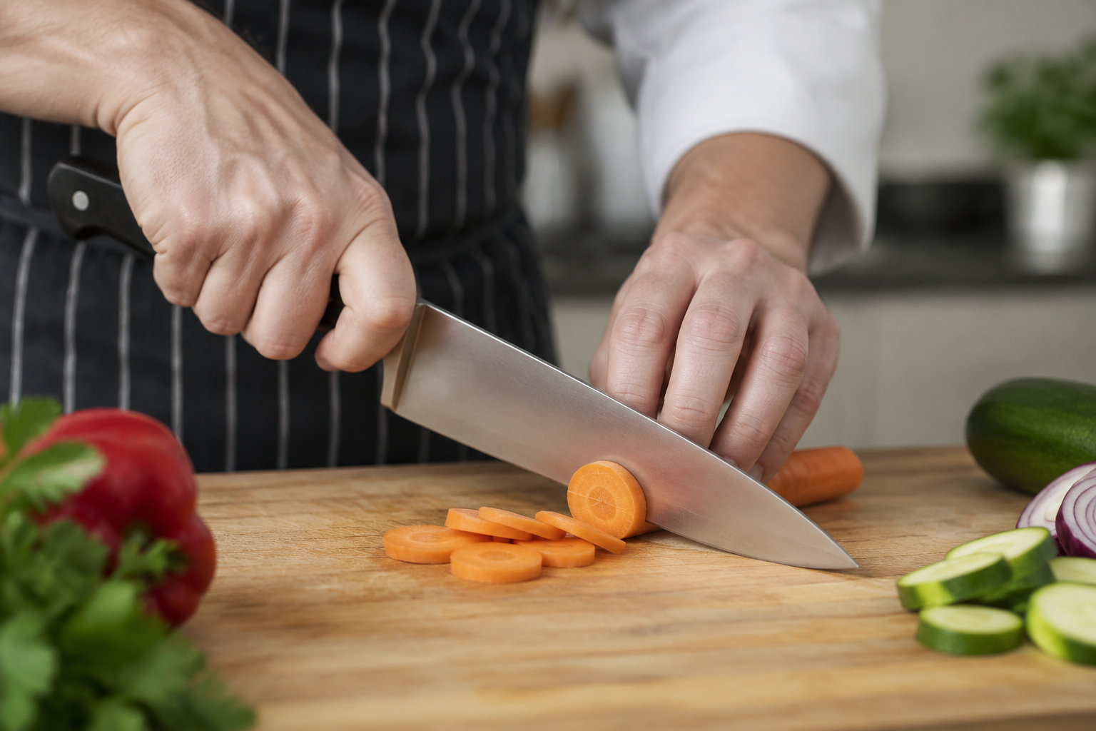 Un gros plan sur une main utilisant la prise en griffe pour couper des légumes sur une planche en bois.