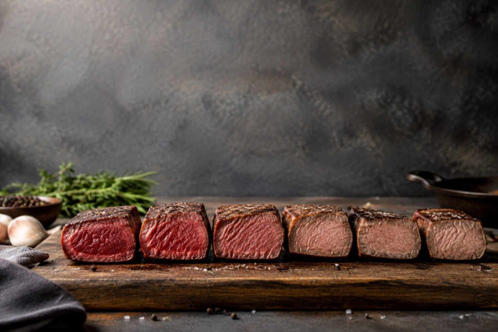Six morceaux de bœuf alignés sur une planche montrant les différents niveaux de cuisson, du bleu au bien cuit.