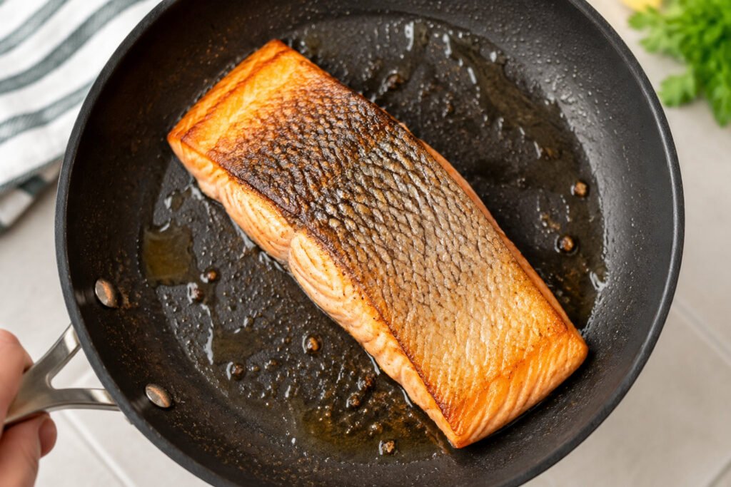 Un pavé de saumon doré cuisant dans une poêle antiadhésive avec une peau bien croustillante.