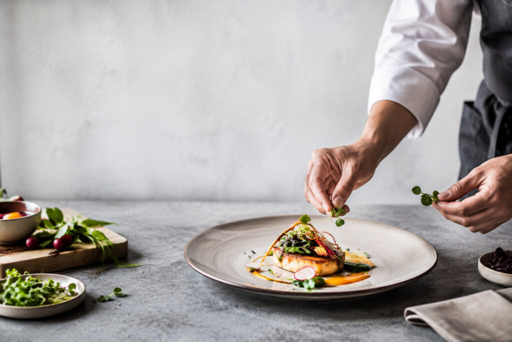 Un chef cuisinier dispose délicatement des herbes fraîches sur une assiette gastronomique élégamment préparée.
